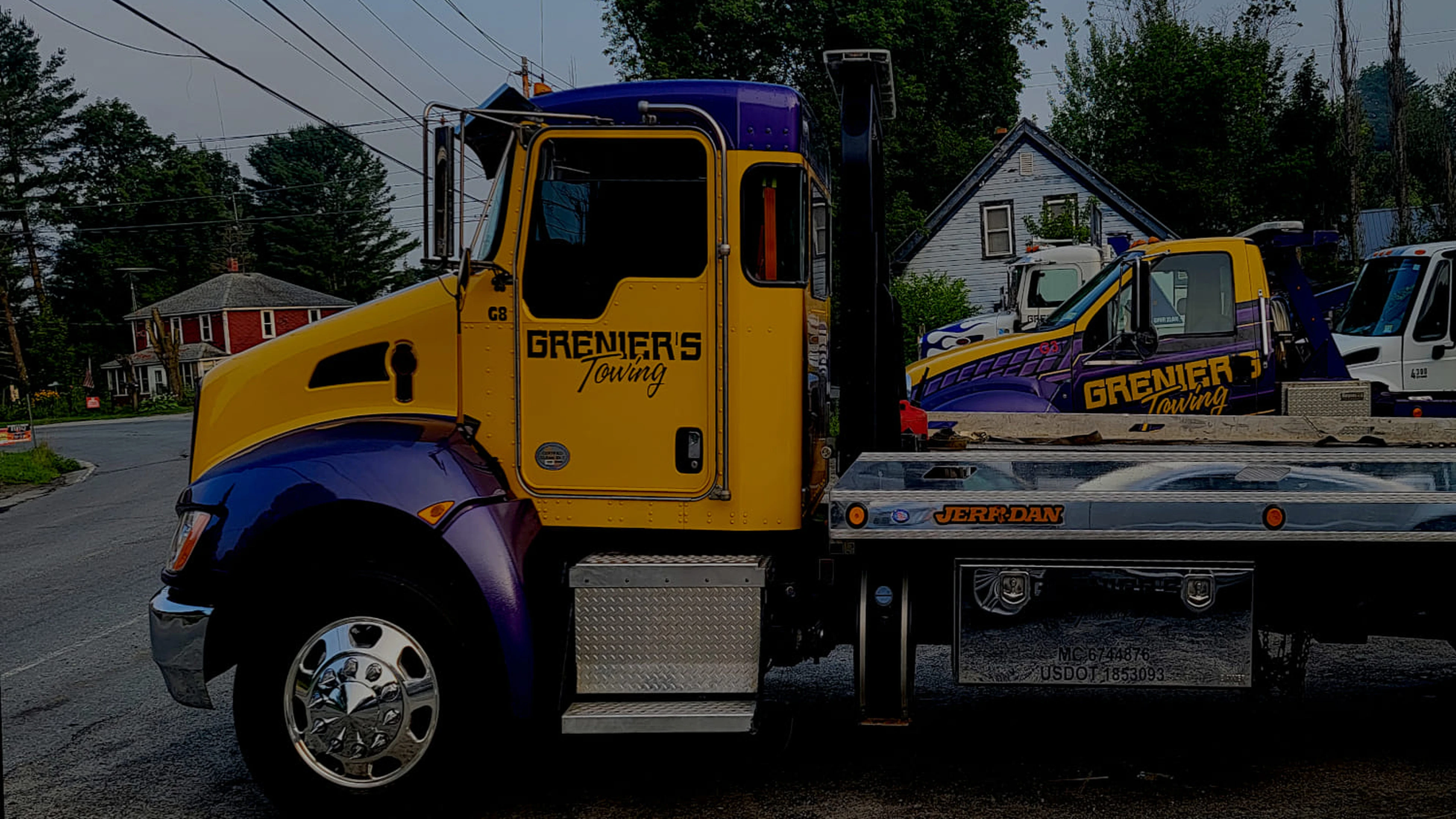 Grenier's Towing yellow and purple branded flatbed truck with GRENIER'S Towing company logo serving local communities across Vermont and New Hampshire